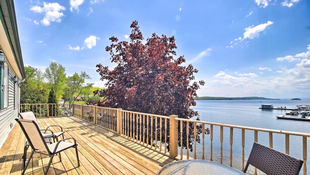 A wooden deck with a glass table and chairs, overlooking a body of water and dock. - Lake Champlain Home w/ Decks, Kayaks & Fire Pit! (Saint Albans City)