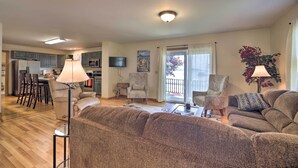 A spacious living room with a large brown sofa, a coffee table, and a TV. There is a kitchen in the background with a dining area. - Lake Champlain Home w/ Decks, Kayaks & Fire Pit! (Saint Albans City)
