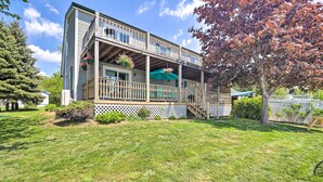 A two-story building with a covered porch, a staircase, and a fenced yard. - Lake Champlain Home w/ Decks, Kayaks & Fire Pit! (Saint Albans City)