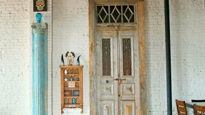 A room with a white brick wall, a wooden door with decorative glass panels, a blue column, and a wooden cabinet with various items. - Oversized loft (Denison)