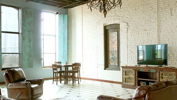A spacious living room with a large TV, leather sofas, a dining area, and a white brick wall. - Oversized loft (Denison)