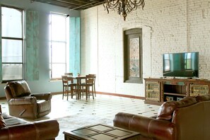 A spacious living room with a large TV, leather sofas, a dining area, and a white brick wall. - Oversized loft (Denison)