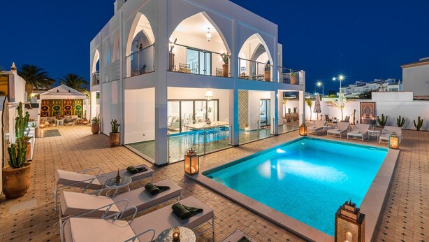 A modern two-story house with a swimming pool, outdoor seating, and a well-lit patio area.