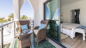 A balcony with wicker chairs, a glass table, and a bed with a white bedspread.