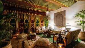 A traditional Moroccan interior with ornate arches, a patterned ceiling, and a cozy seating area with cushions and lanterns.