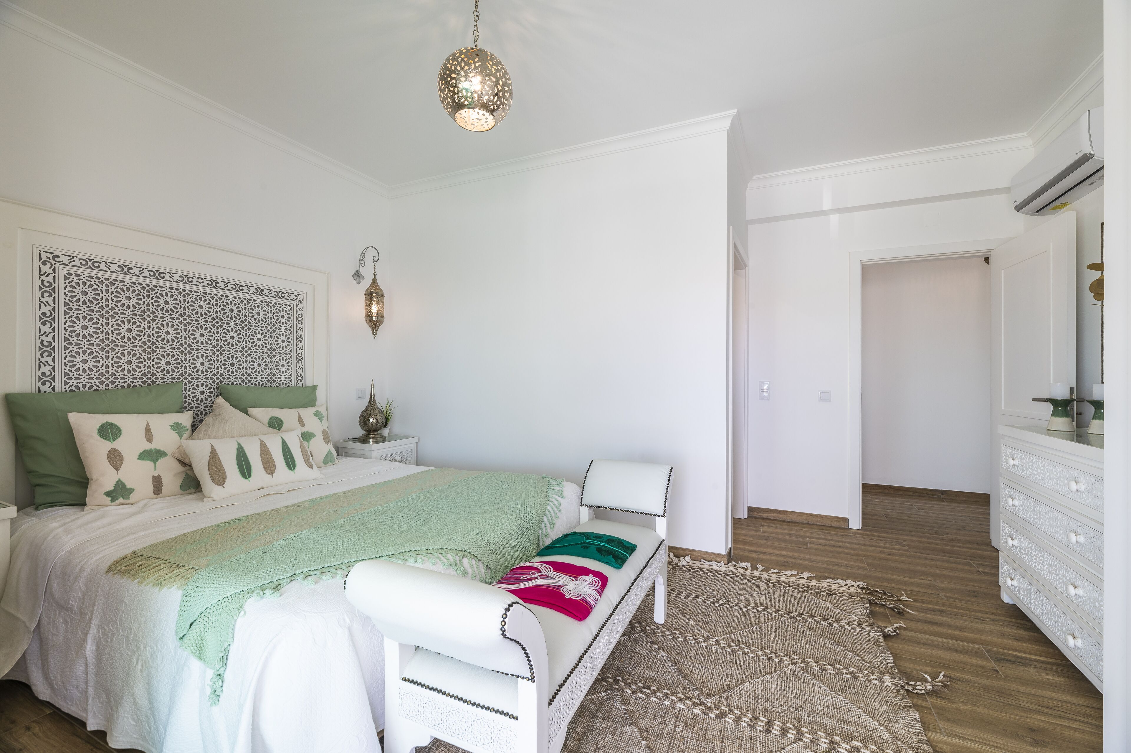 A bedroom with a bed, a nightstand, a wall-mounted lamp, and a patterned rug.