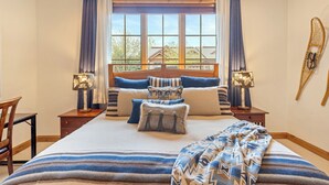 Une chambre avec un grand lit, deux tables de chevet, une chaise, une fenêtre avec des rideaux et une planche de surf accrochée au mur.