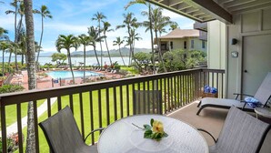 Un balcon avec une table en verre, deux chaises et une vue sur une piscine et des palmiers.