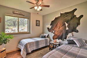 Un dormitorio con dos camas, un ventilador de techo, un ventanal grande y un cuadro de cuero de vaca colgado en la pared.