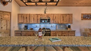 A kitchen with wooden cabinets, a granite countertop, a stainless steel microwave, and a chandelier.