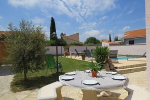 Enjoy dining al fresco in a serene outdoor setting surrounded by lush greenery and a nearby swimming pool.
