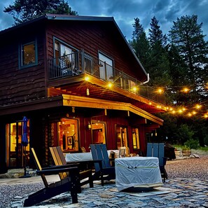A wooden cabin with a balcony, outdoor seating, and string lights. - Serene Glacier Cabin With River and Mountain Views.  (Columbia Falls)