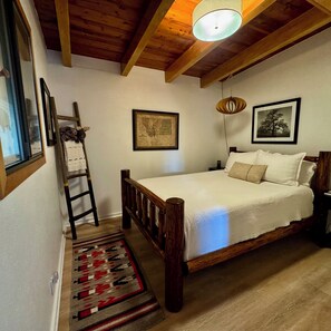 A bedroom with a wooden bed, a ladder, a framed map, and a hanging light fixture. - Serene Glacier Cabin With River and Mountain Views.  (Columbia Falls)