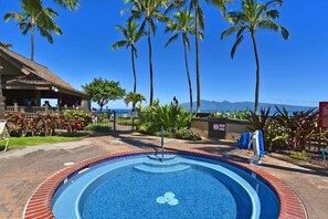 A swimming pool with a tiled edge, surrounded by palm trees and a building with a tiled roof.