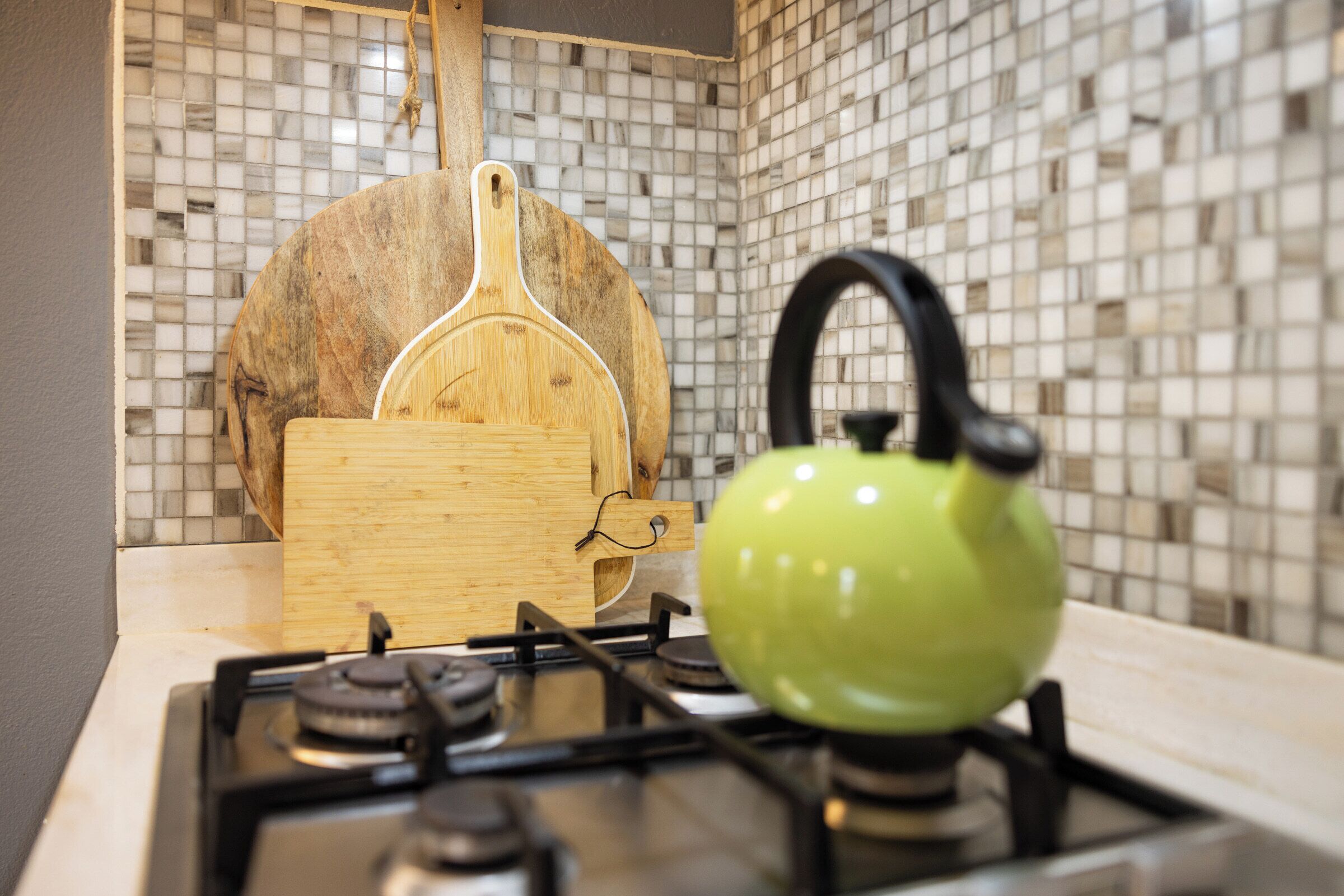 Una cucina con piano cottura a gas, bollitore verde e tagliere in legno.