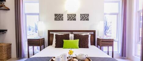 A neatly made bed with a tray of breakfast items, a green pillow, and decorative wall art.