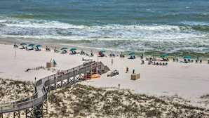 Una playa con un paseo marítimo de madera que conduce a una estación de salvavidas, rodeada de sillas y sombrillas de playa.