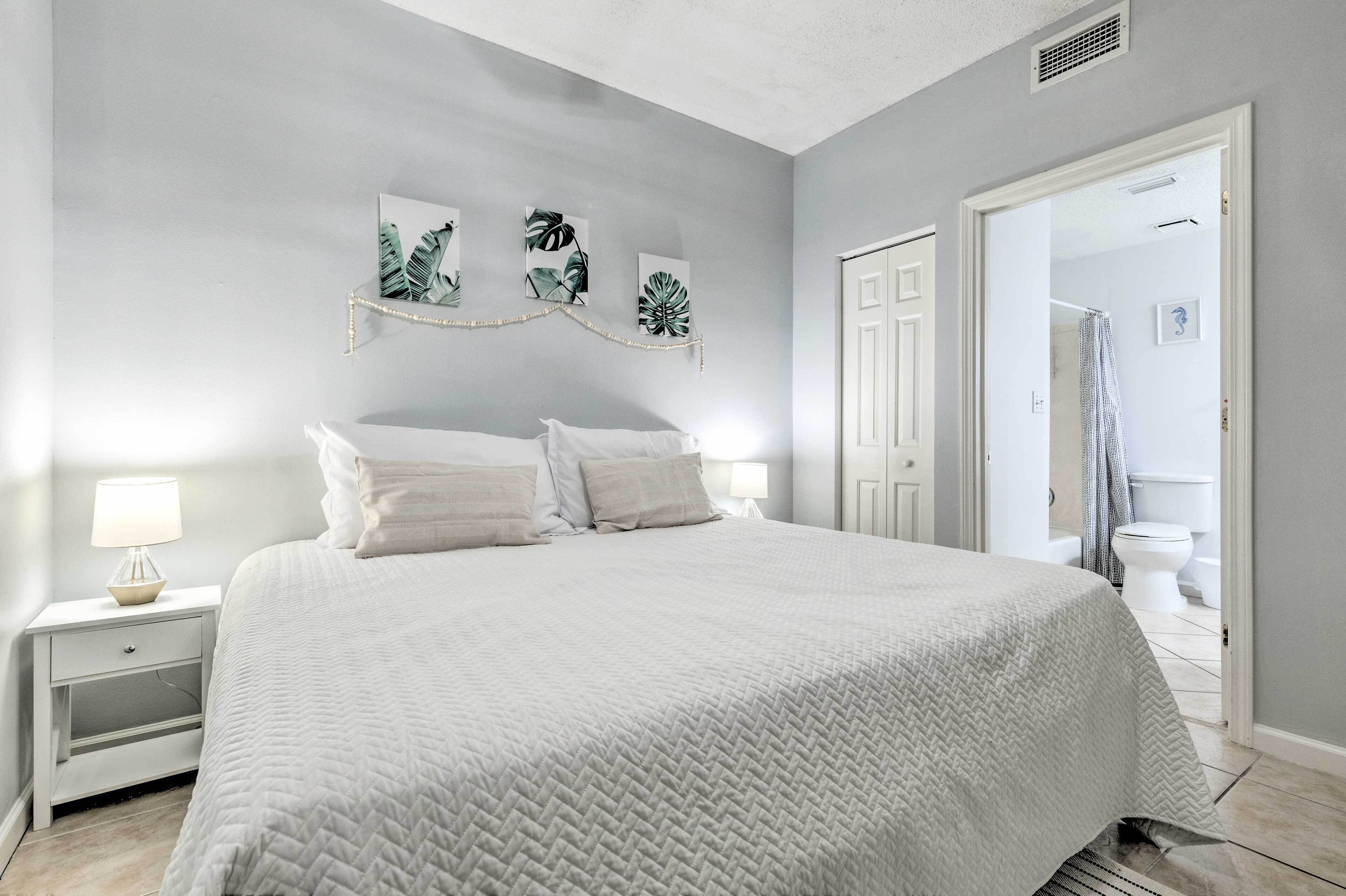 Une chambre à coucher avec un grand lit, une table de chevet avec une lampe et une porte donnant sur une salle de bain.