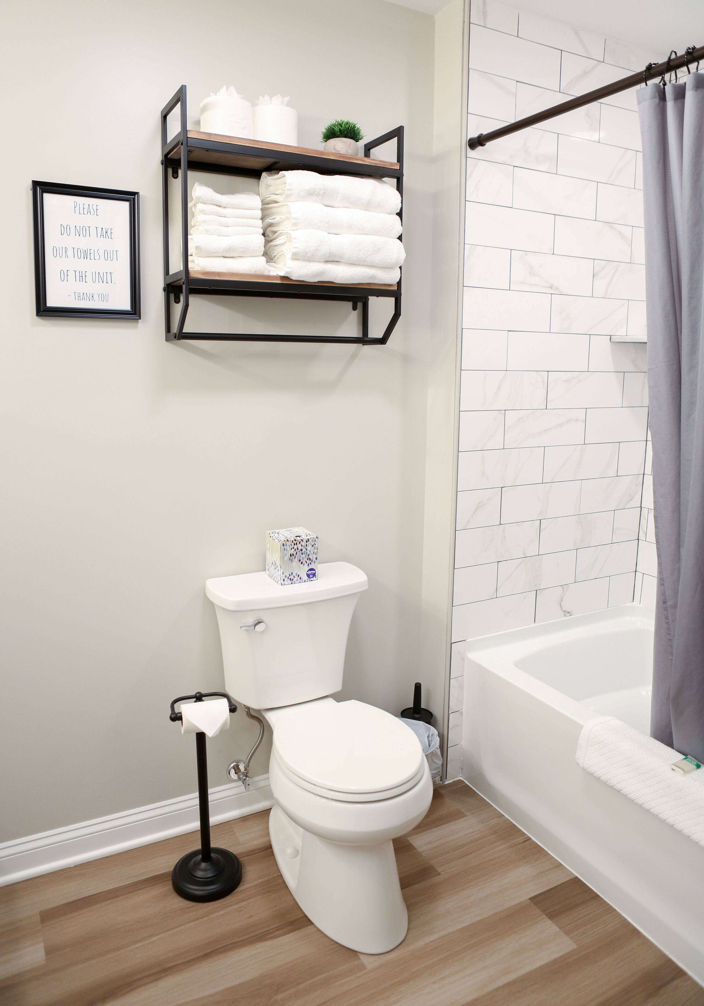 A modern bathroom with a toilet, a shelf with towels, a framed sign, and a shower curtain.