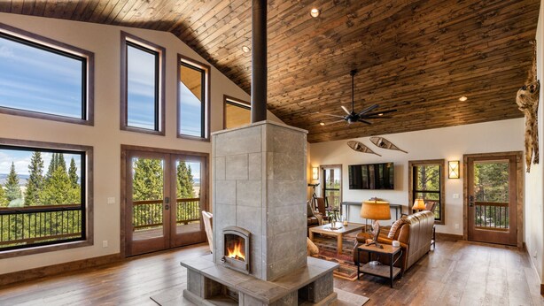 Amplia sala de estar con chimenea de piedra, ventanas grandes y techo de madera.