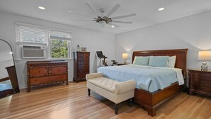 A bedroom with a large bed, a ceiling fan, a dresser, a chair, and a nightstand. - Tranquil 1875 Victorian with beautiful grounds and inground pool (South Kingstown)