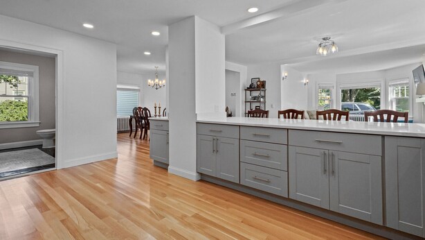 A modern kitchen with grey cabinets, a white countertop, and a dining area with wooden chairs. - Tranquil 1875 Victorian with beautiful grounds and inground pool (South Kingstown)