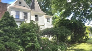 A two-story house with a steeply pitched roof and a visible chimney. - Tranquil 1875 Victorian with beautiful grounds and inground pool (South Kingstown)