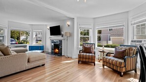 A spacious living room with a fireplace, a television, and a view of the outside. - Tranquil 1875 Victorian with beautiful grounds and inground pool (South Kingstown)