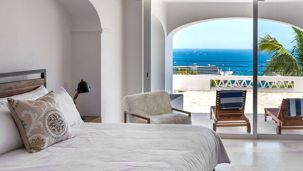 A bedroom with a large bed, a chair, and a view of the ocean.
