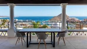 A balcony with a table and chairs, overlooking a coastal cityscape with a prominent mountain and marina.