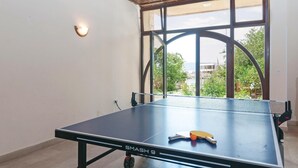 Une table de ping-pong portant l’inscription « SMASH 9 », dans une pièce dotée d’une grande fenêtre, d’un luminaire fixé au mur et offrant une vue sur la verdure à l’extérieur.