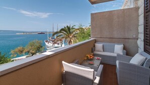 Un balcon agrémenté de meubles en osier, d’un panier de fruits et offrant une vue sur la mer et les bateaux.