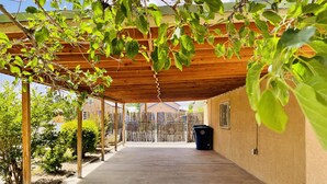 A covered patio area with a concrete floor, wooden pergola, and a view of a fenced backyard.