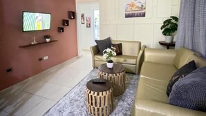 Ett vardagsrum med en beige soffa, två runda sidobord i trä, en tv som är monterad på väggen och en krukväxt.