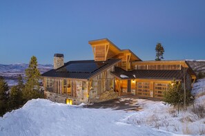 A large, multi-story log cabin with a stone foundation, large windows, and a garage.