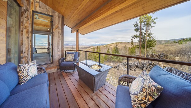 A wooden deck with a glass door leading to a balcony, furnished with blue sofas and a table with a fire pit. - Colorado's Coolest Ski In/Out Home - World Class Mtn. Biking, Hiking & Fishing (Granby)