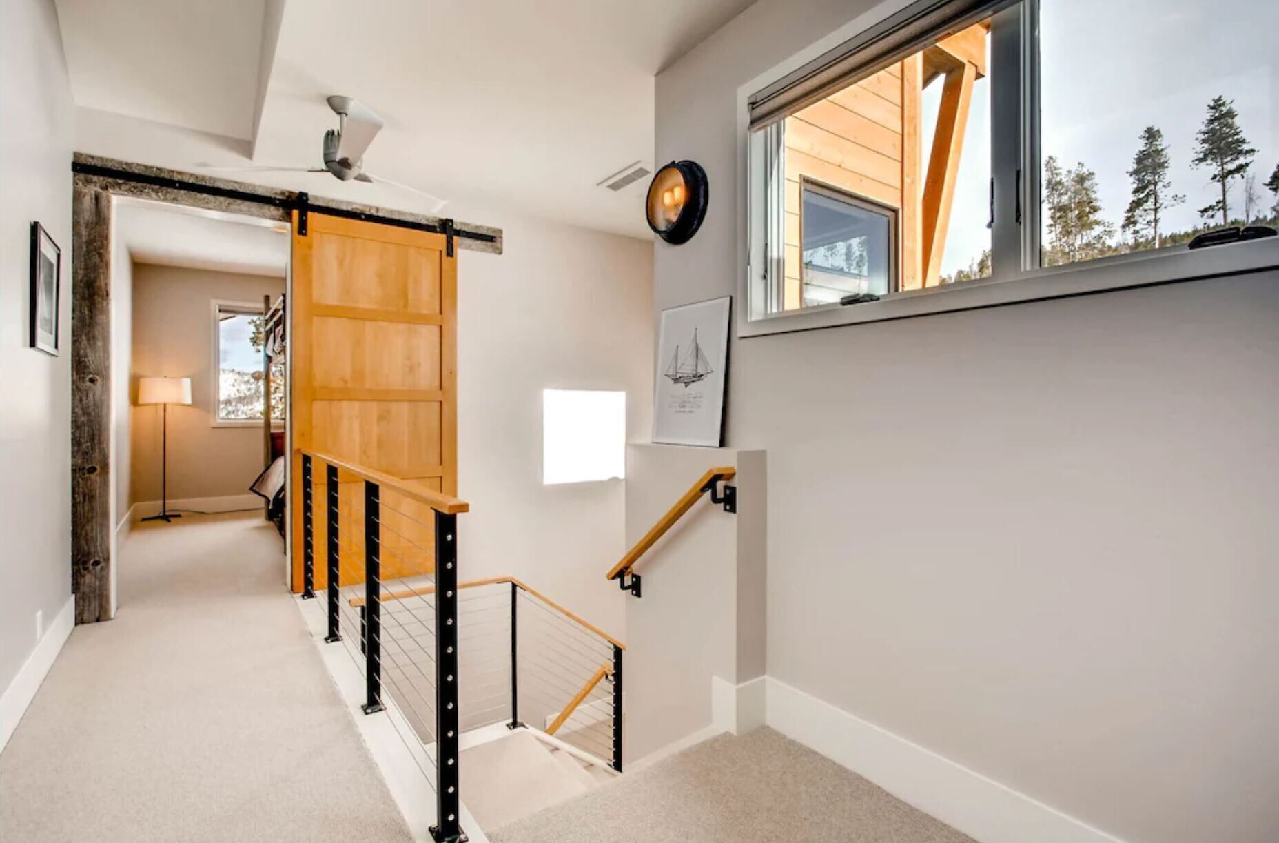 A staircase with wooden handrails and a black metal railing, leading to a room with a window overlooking trees.