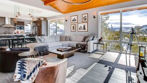 A modern living room with a large sectional sofa, a coffee table, and a view of mountains through large windows. - Colorado's Coolest Ski In/Out Home - World Class Mtn. Biking, Hiking & Fishing (Granby)