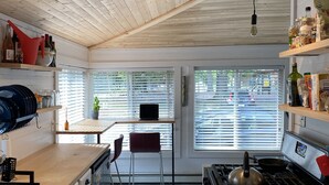 Een keuken met houten plafond, een fornuis, een spoelbak en een eethoek met een stoel en tafel.