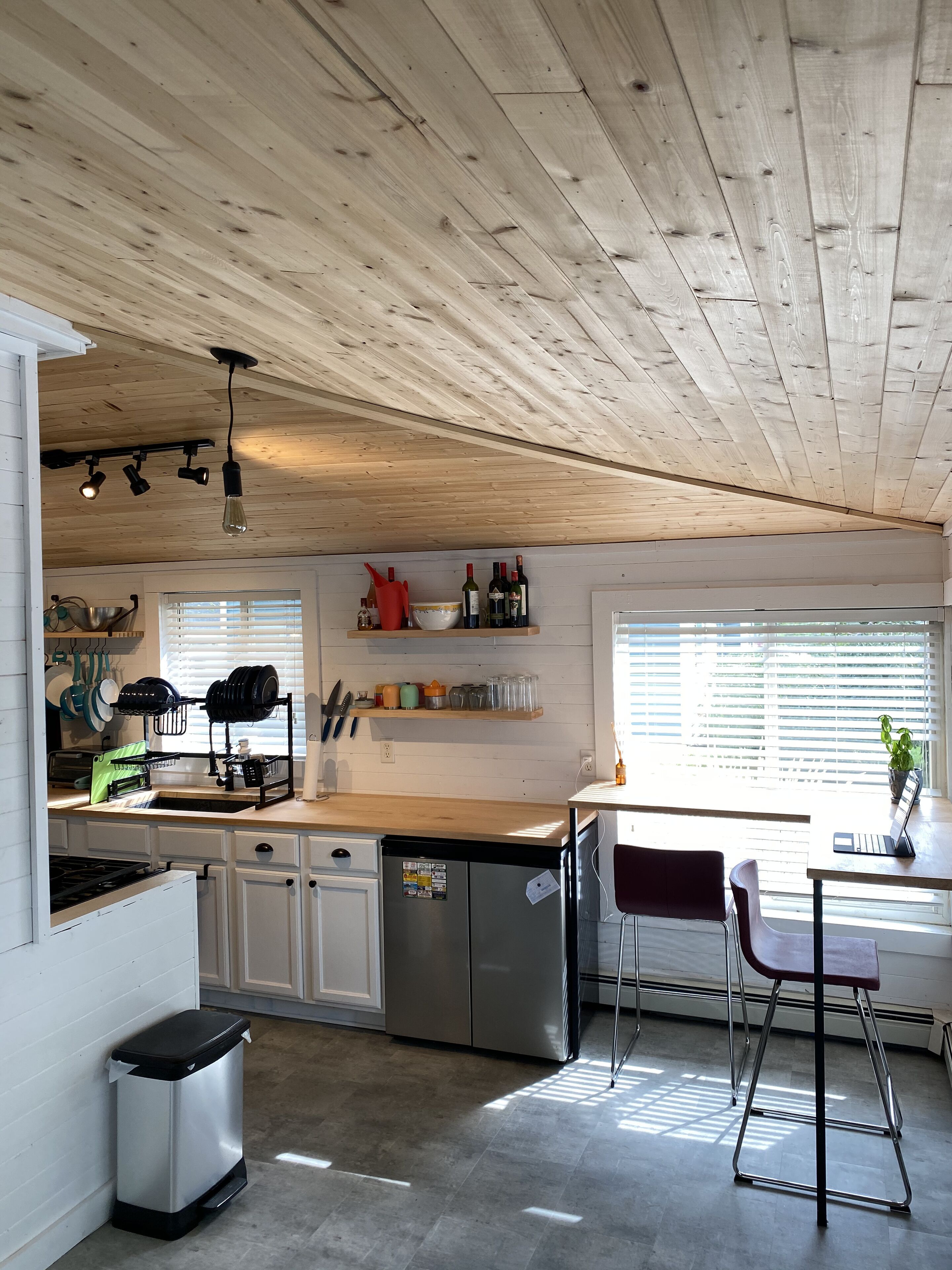 A modern kitchen with wooden ceiling, built-in appliances, and a dining area with a chair and table.