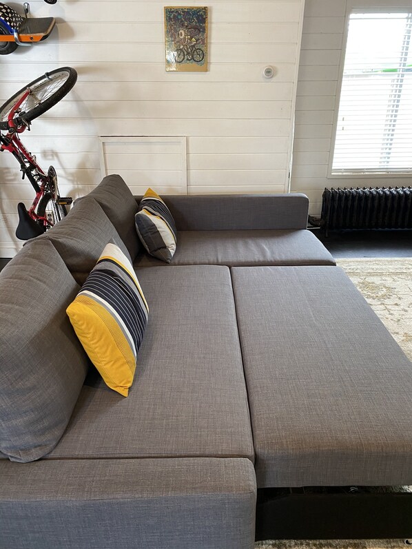 A grey sectional sofa with multiple cushions, a bicycle leaning against the wall, and a radiator. - Beautiful cozy cottage 1 block from the lake and Oakwood hotel. (Syracuse)