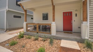 Ein modernes, zweistöckiges Haus mit roter Tür, überdachter Veranda und kleinem Garten mit Kies und Pflanzen.