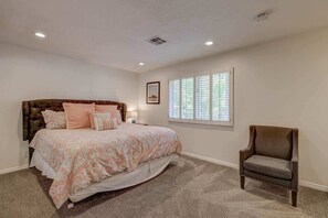A bedroom with a large bed, a chair, and a window with blinds.
