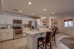 A modern kitchen with white cabinets, stainless steel appliances, and a central island with bar stools. - Las Palmas Resort #1620 | All-Inclusive Amenities (Saint George)