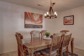 A dining room with a wooden table and chairs, a chandelier, and two framed artworks on the walls. - Las Palmas Resort #1620 | All-Inclusive Amenities (Saint George)