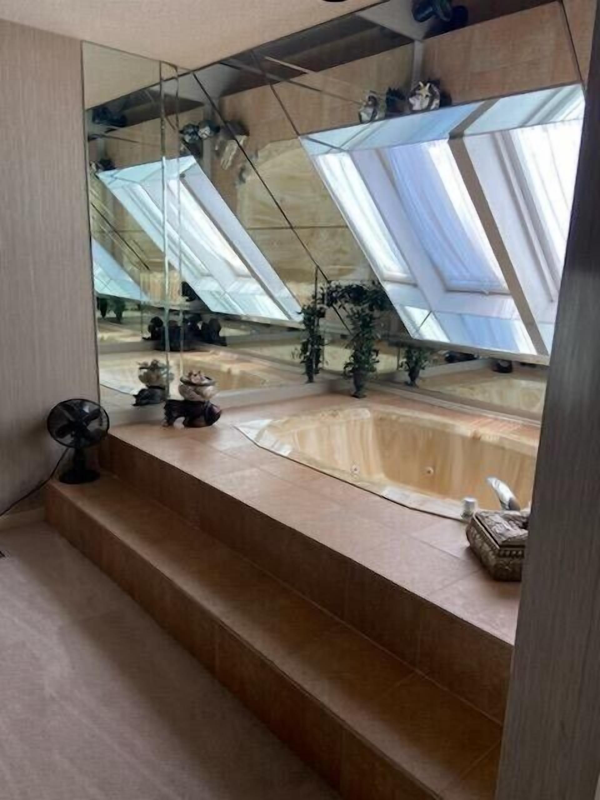 A modern bathroom with a large mirror, a bathtub, and a fan.