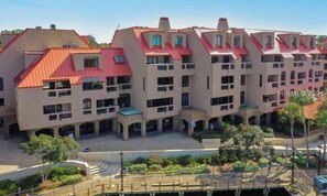 A multi-story residential building with a red roof, multiple balconies, and a central courtyard with greenery.
