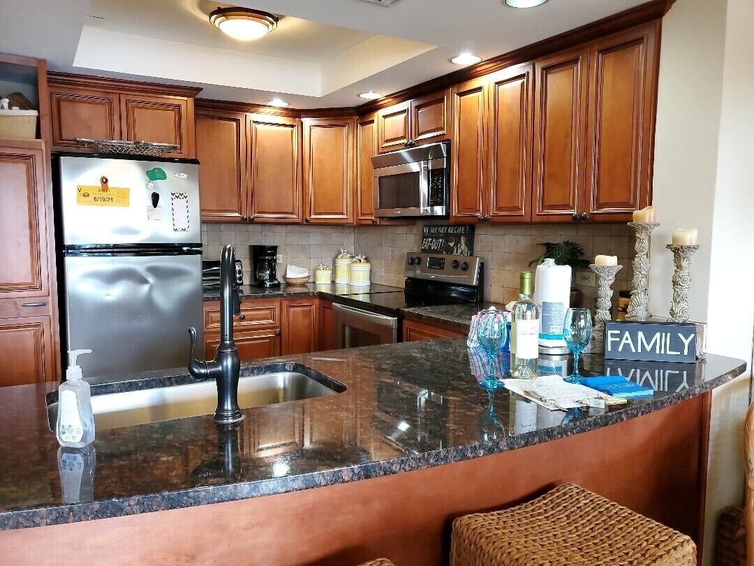 Una cocina con armarios de madera, electrodomésticos de acero inoxidable, encimera de granito y un letrero que dice 'FAMILY'.