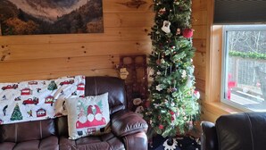 Un interno accogliente con un divano in pelle, un tavolino da caffè con decorazioni natalizie, un albero di Natale e un dipinto di un paesaggio montano.