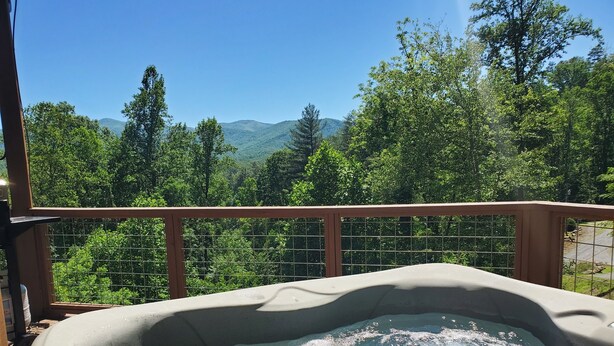 Una vasca idromassaggio con un pontile in legno e una ringhiera in metallo, immersa nel verde e con montagne sullo sfondo.